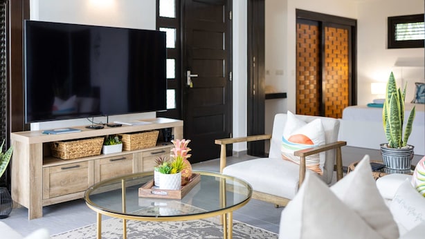A modern living room with a flat-screen TV, wooden furniture, and a glass coffee table. - Indigo Garden at Blue Bay Golf Beach Resort (Sint Michiel)