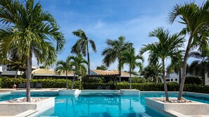 A swimming pool surrounded by palm trees and a building with a tiled roof. - Indigo Garden at Blue Bay Golf Beach Resort (Sint Michiel)