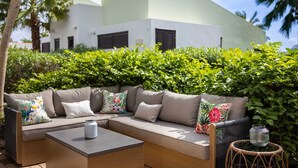 A modern outdoor seating area with a sofa, a table, and a wicker side table. - Indigo Garden at Blue Bay Golf Beach Resort (Sint Michiel)