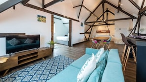 Un espacio habitable moderno estilo loft, con vigas de madera a la vista, un televisor grande, un sofá y un comedor.