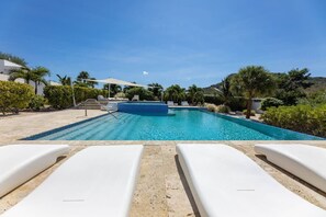 A swimming pool with lounge chairs, surrounded by greenery and a clear sky. - Green View Delight Chic Blue Bay Apartment (Sint Michiel)