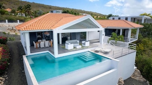 Et moderne hus med swimmingpool, udendørs møbler og et poolområde med terrasser.