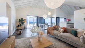 A modern living room with a large window, a sofa, a coffee table, and a dining area.