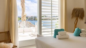 A hotel room with a bed, towels, a view of the sea, and a balcony with a chair and umbrella. - Tropical Luxury Private Beach La Villa Blanca (Jan Thiel)