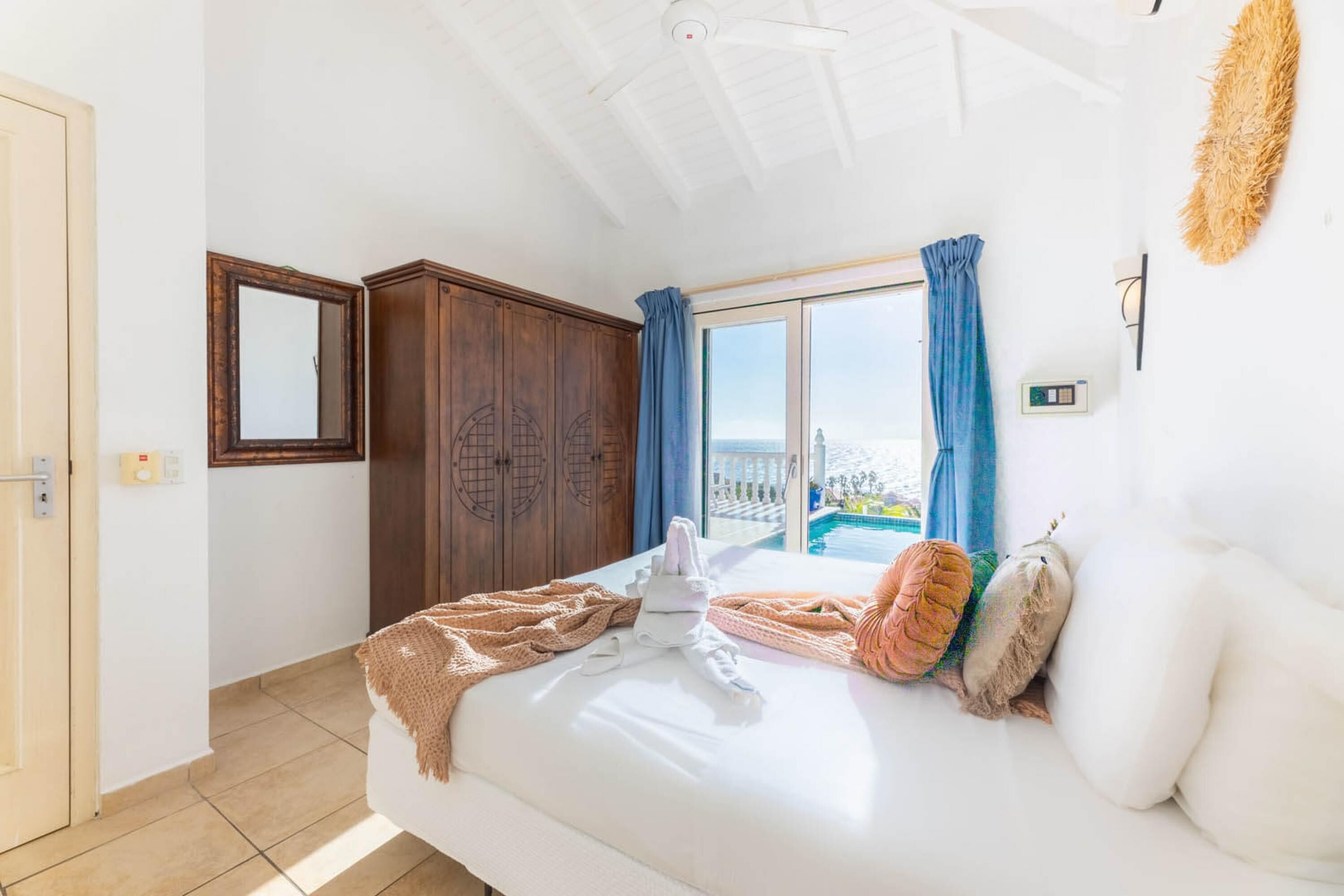 A bedroom with a bed, a wardrobe, a window with curtains, and a view of a pool.