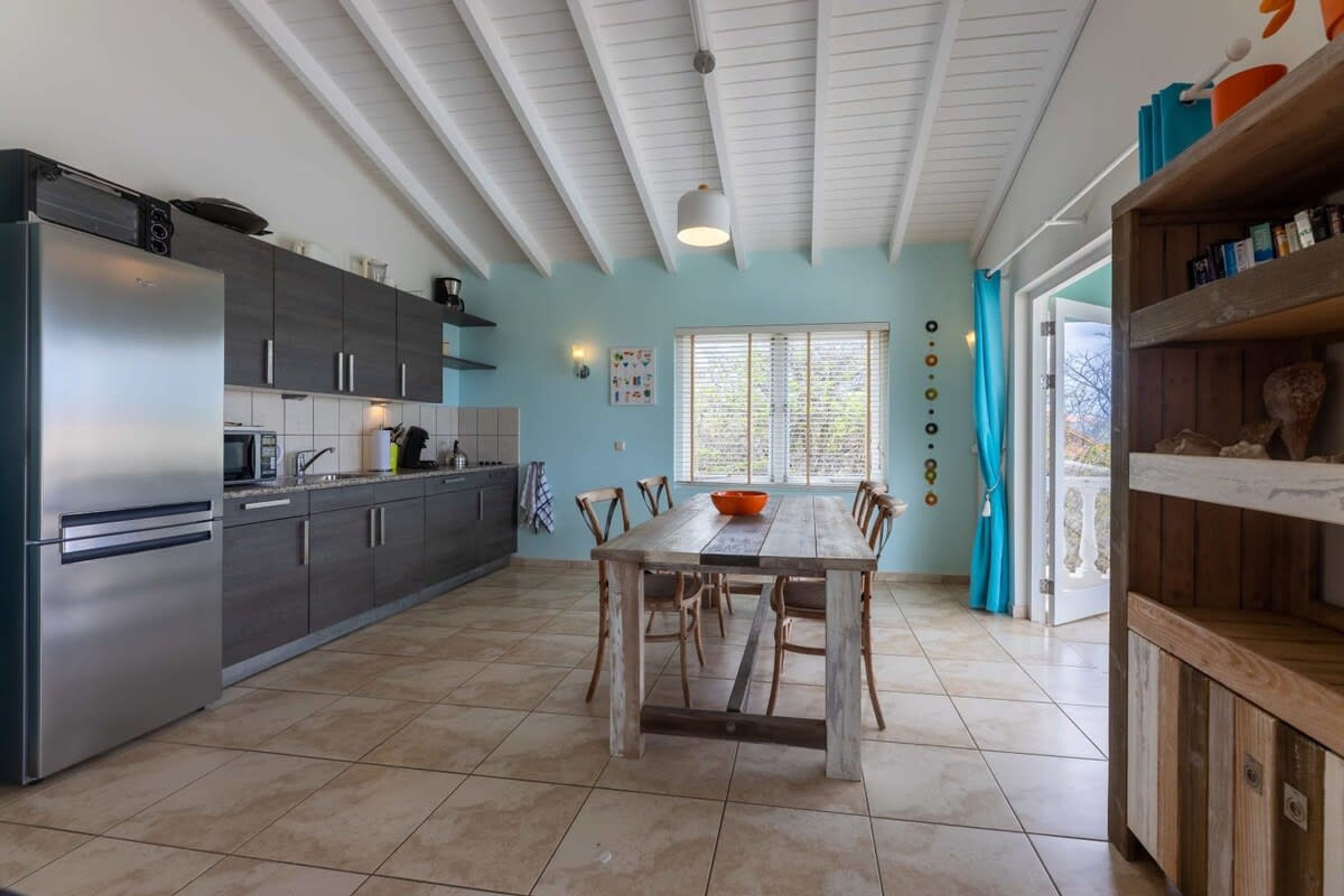 A modern kitchen with a large island, dark cabinets, and a dining area with a wooden table and chairs.
