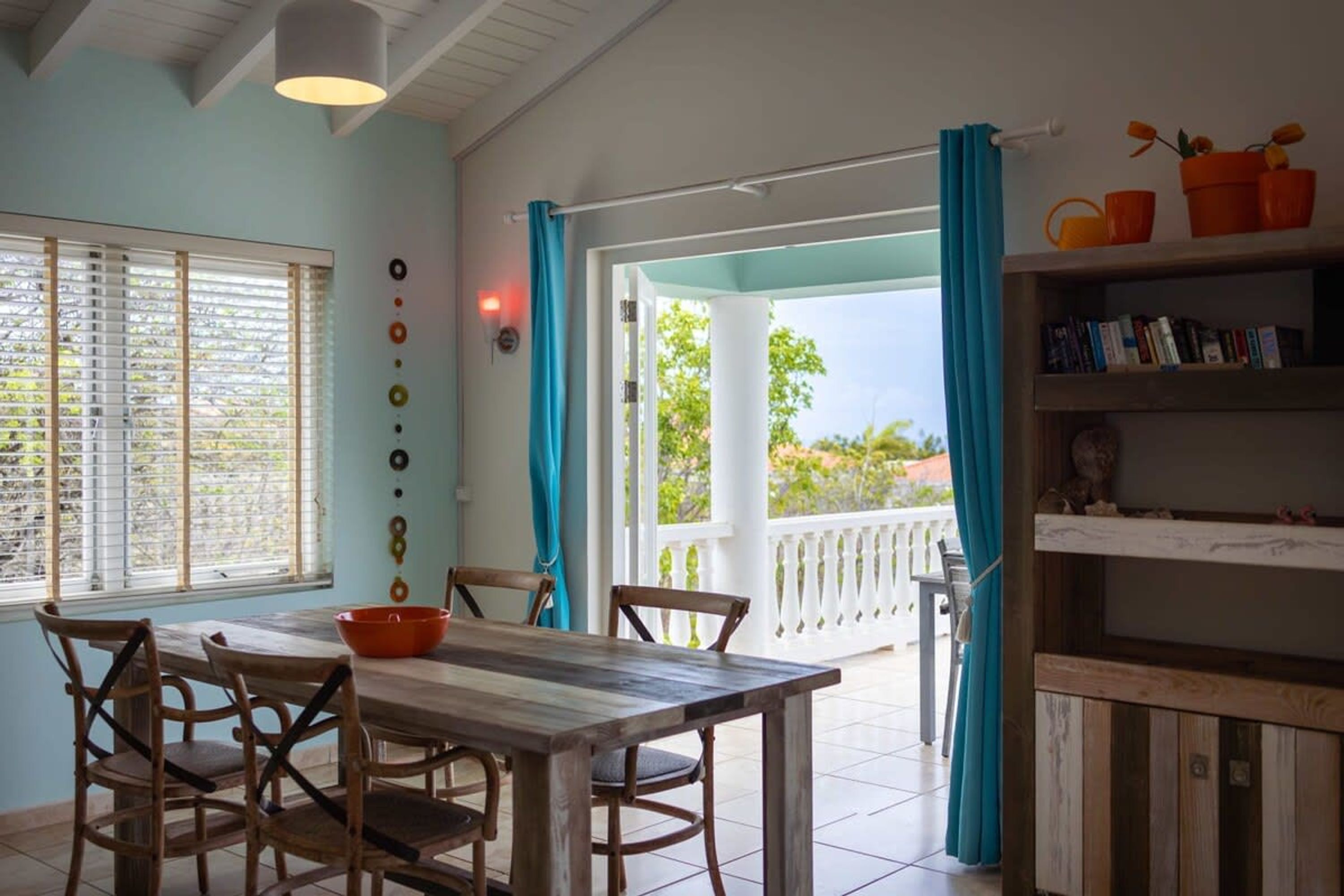 A dining area with a wooden table and chairs, a bowl, and a bookshelf with books and decorative items.