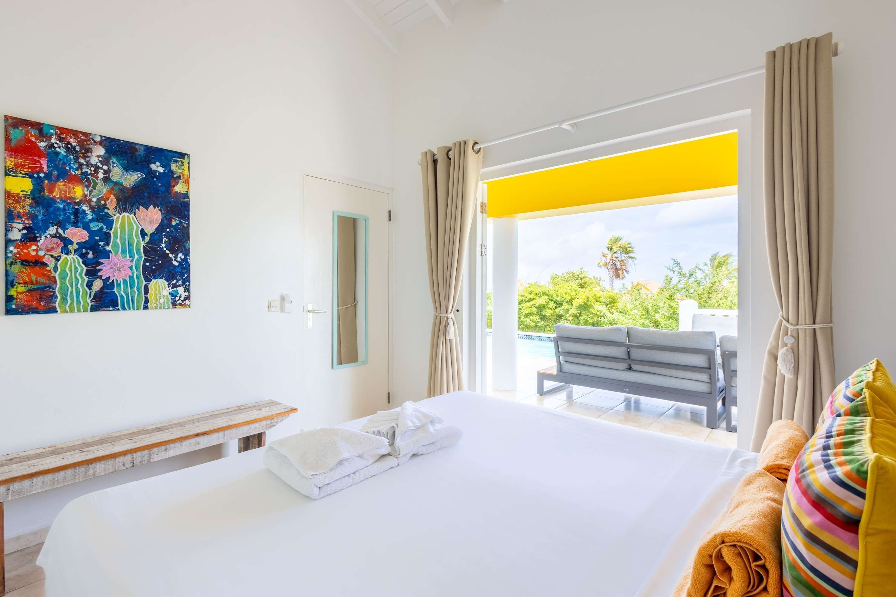 A hotel room with a bed, a bench, a painting, and a balcony with a view.