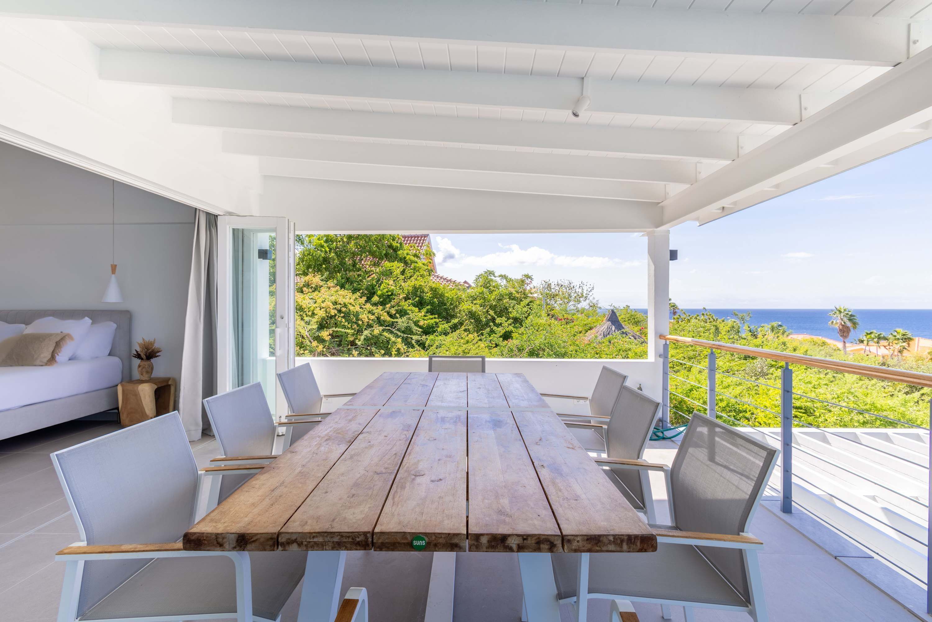 A wooden table with white chairs in a modern, open-plan living area with a view of the sea.