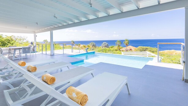 A poolside area with lounge chairs and a view of the ocean. - Coral Dreams Ocean Whispers at Villa Solaris (St. Marie)