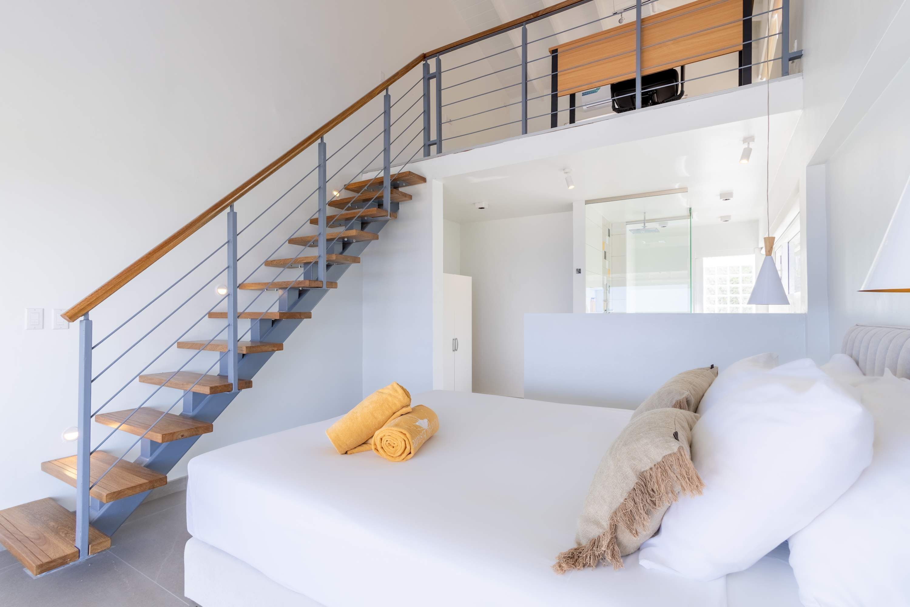 Une chambre avec un escalier en bois, un lit avec une literie blanche et une grande fenêtre.