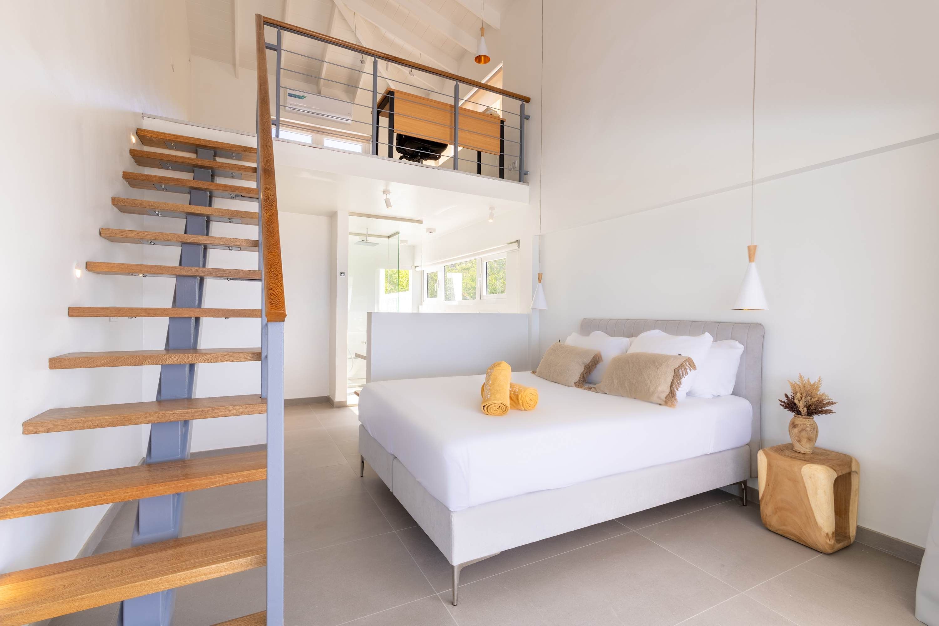 A modern bedroom with a large bed, a wooden staircase, and a view of a bright room.