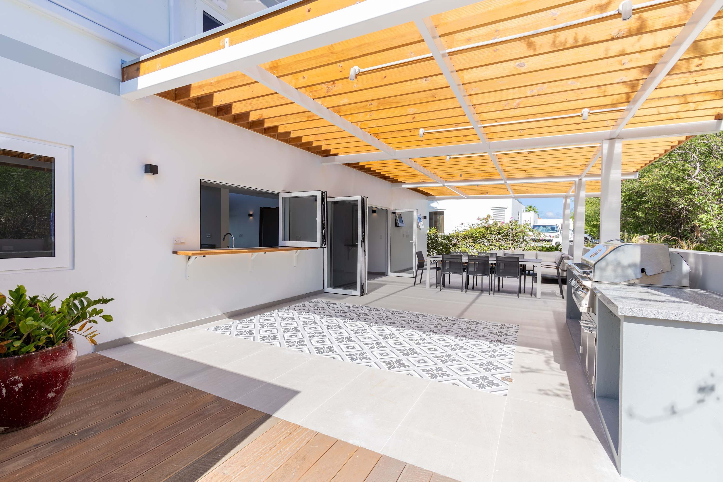 An outdoor patio with a wooden pergola, a grill station, and a dining area with a table and chairs.