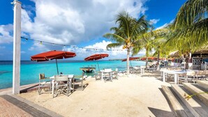 A beachside café with outdoor seating, palm trees, and a view of the ocean. - Coral Dreams Ocean Whispers at Villa Solaris (St. Marie)