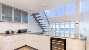 A modern kitchen with a built-in wine cooler, a stainless steel staircase, and large windows offering a view of the ocean. - Coral Dreams Ocean Whispers at Villa Solaris (St. Marie)