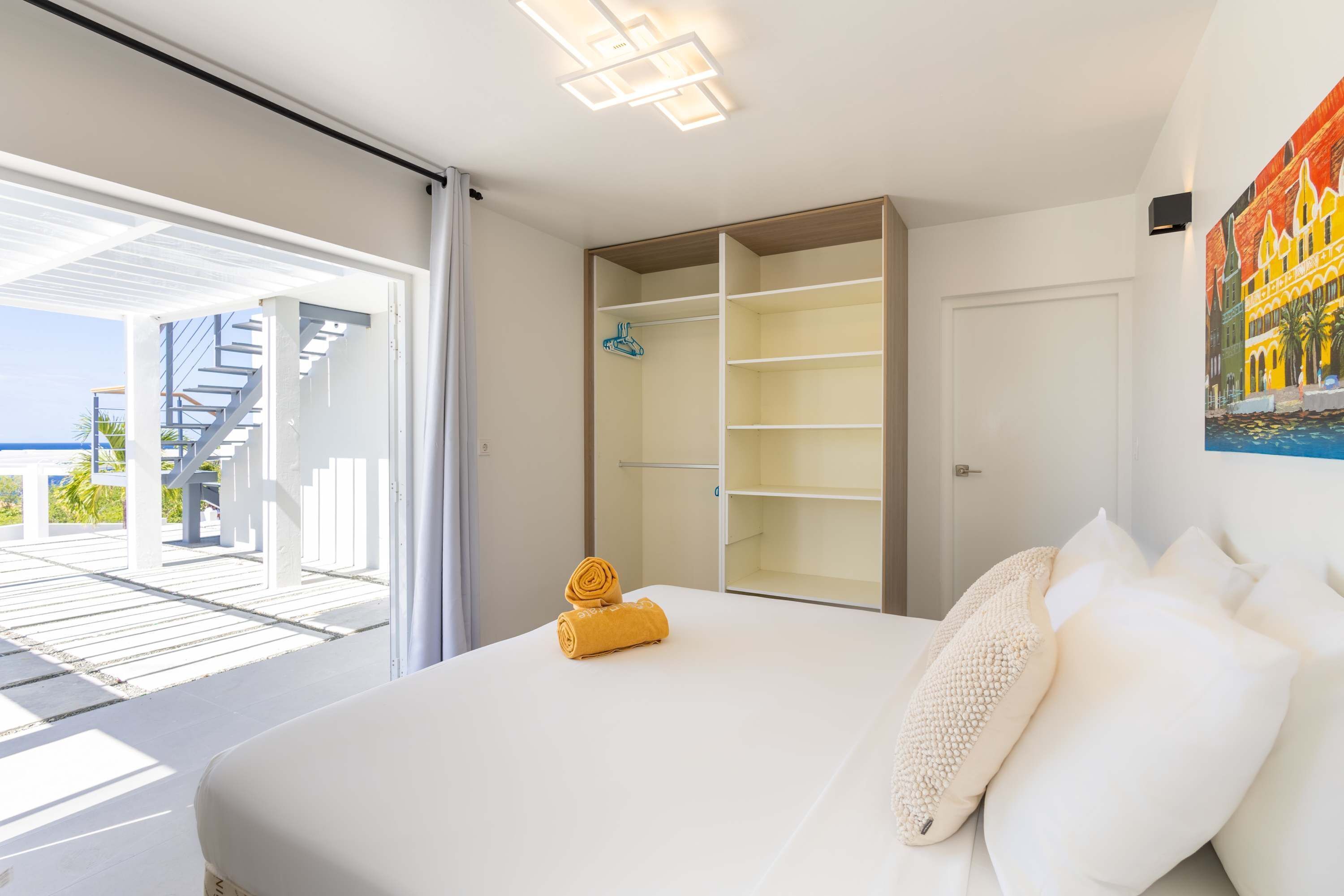 A modern bedroom with a large bed, a walk-in closet, and a view of the outdoor deck.