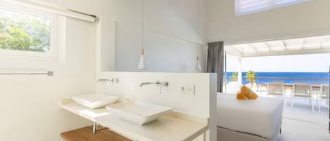 A modern bathroom with a large window, a wooden vanity, and a bed with a view of the ocean.