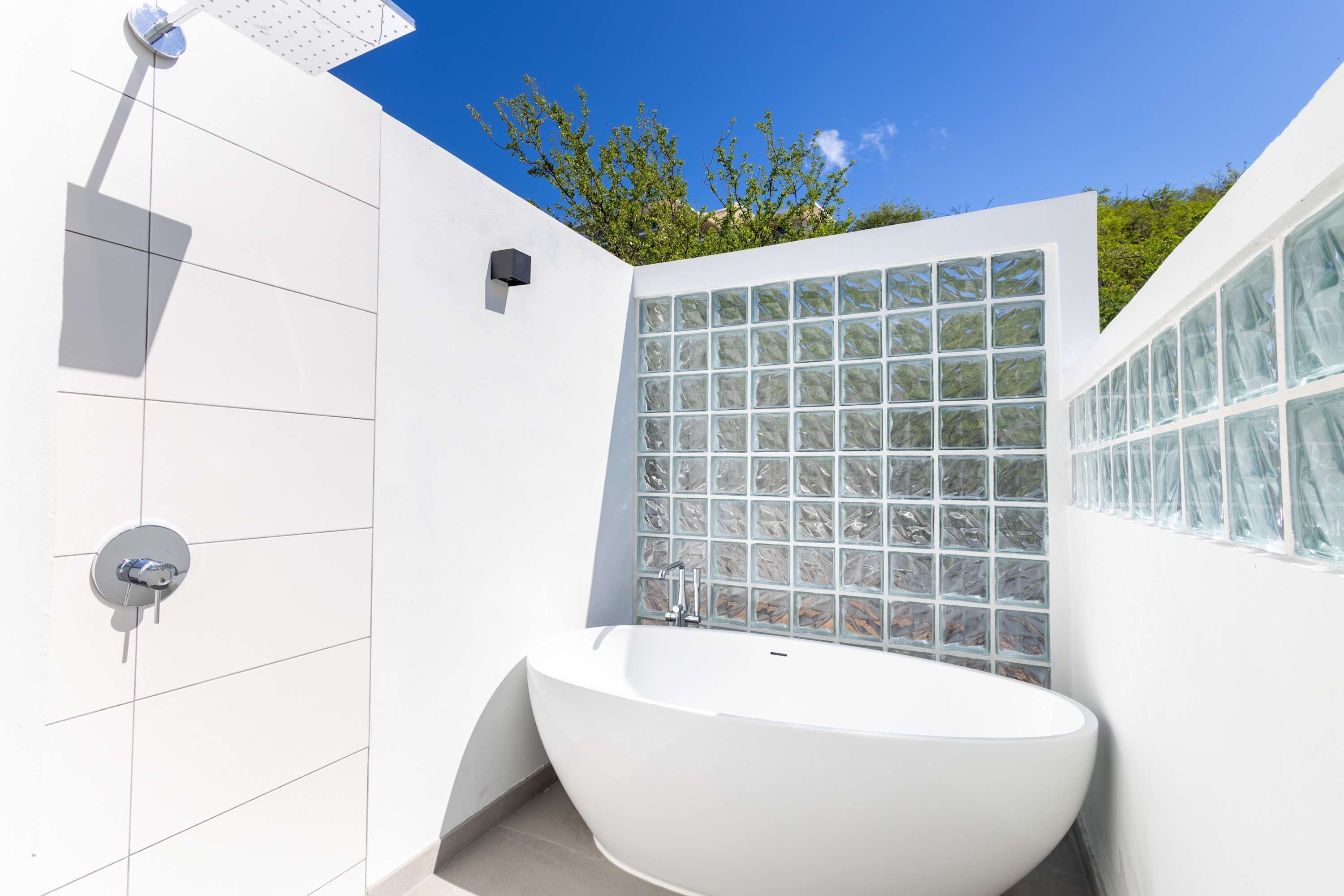 Un baño moderno con una bañera independiente, paredes con azulejos y cabina de ducha con bloques de vidrio.