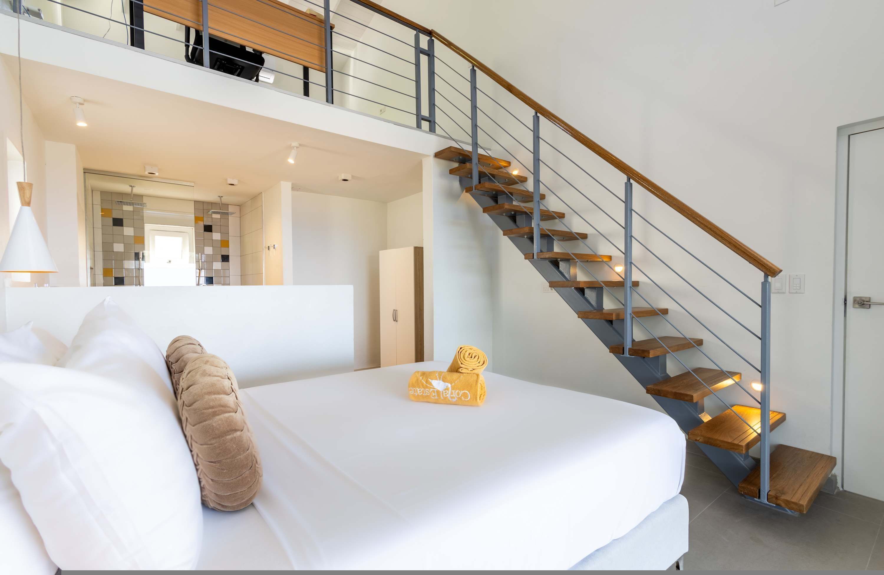 Quarto de hotel moderno com uma cama grande, uma escada de madeira e vista para o corredor.