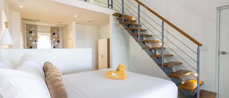 Quarto de hotel moderno com uma cama grande, uma escada de madeira e vista para o corredor.