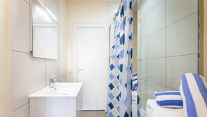 A bathroom with a white sink, a mirror, a shower curtain with a blue pattern, and a towel rack with folded towels. - Charming 2BR Apt With Tropical Garden Pool (Sint Michiel)