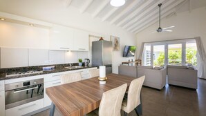 A modern kitchen with white cabinets, a wooden dining table, and a built-in oven. - Charming 2BR Apt With Tropical Garden Pool (Sint Michiel)
