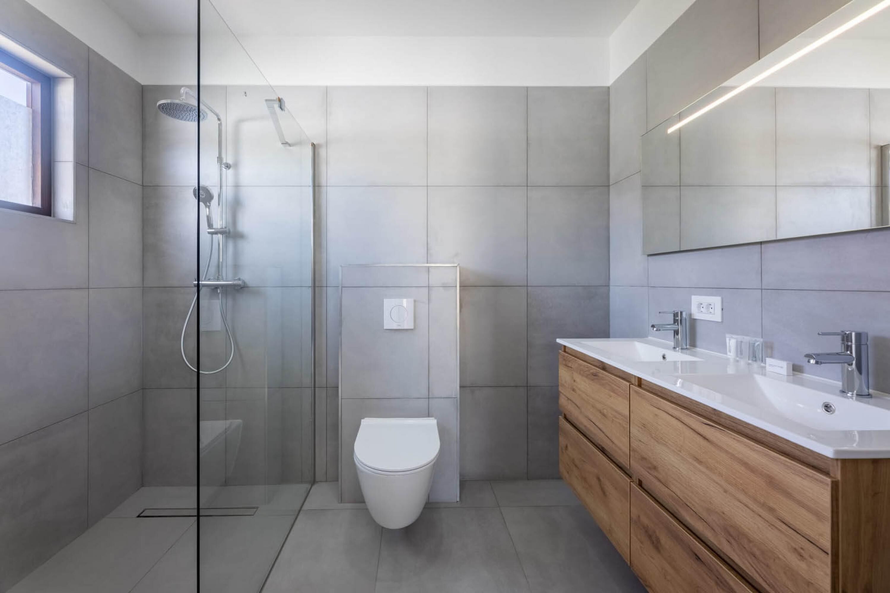 Un baño moderno con ducha envuelta en vidrio, inodoro blanco y tocador de madera con un espejo grande.