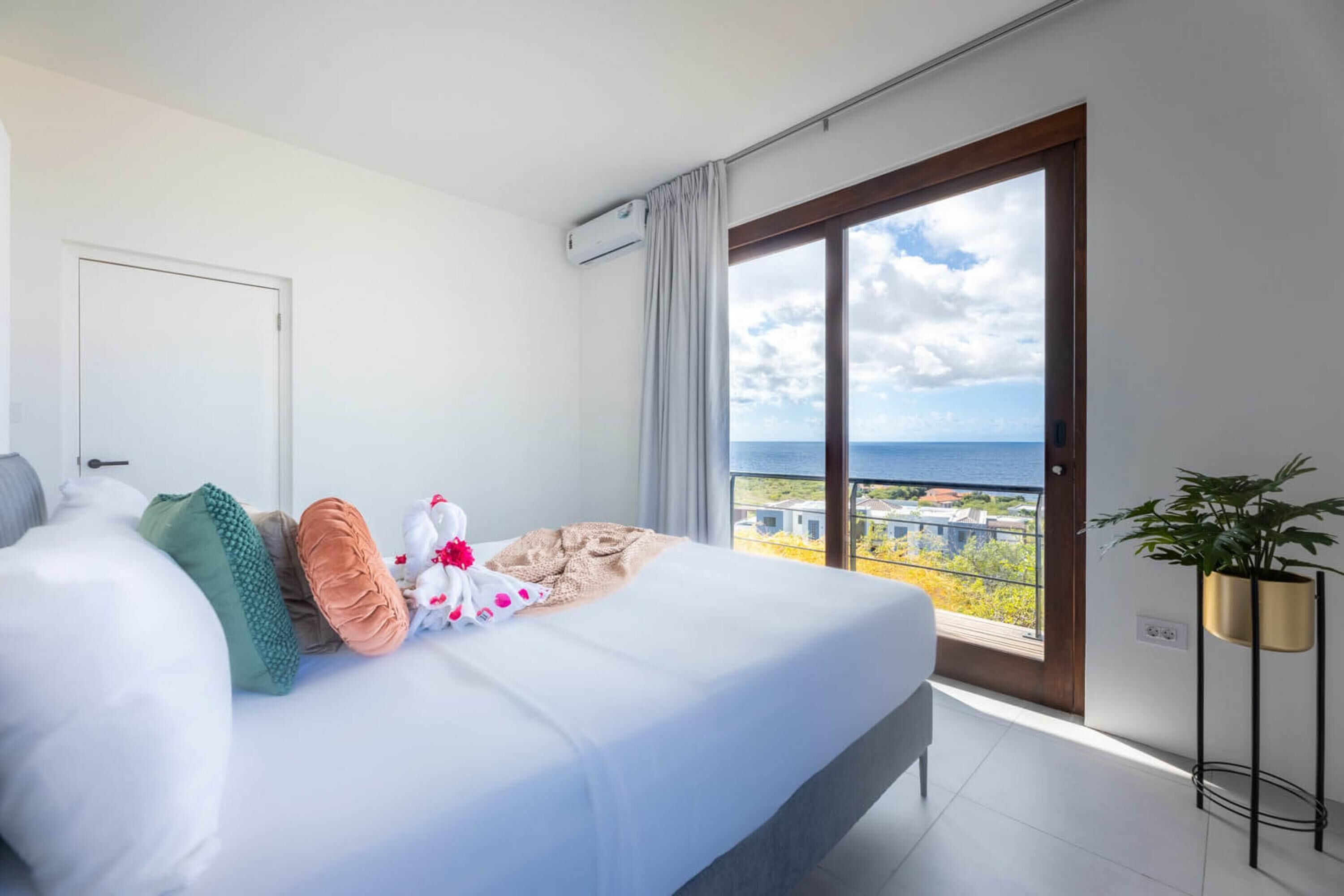 Une chambre d’hôtel avec un grand lit, une vue sur la mer et un balcon agrémenté d’une plante en pot.