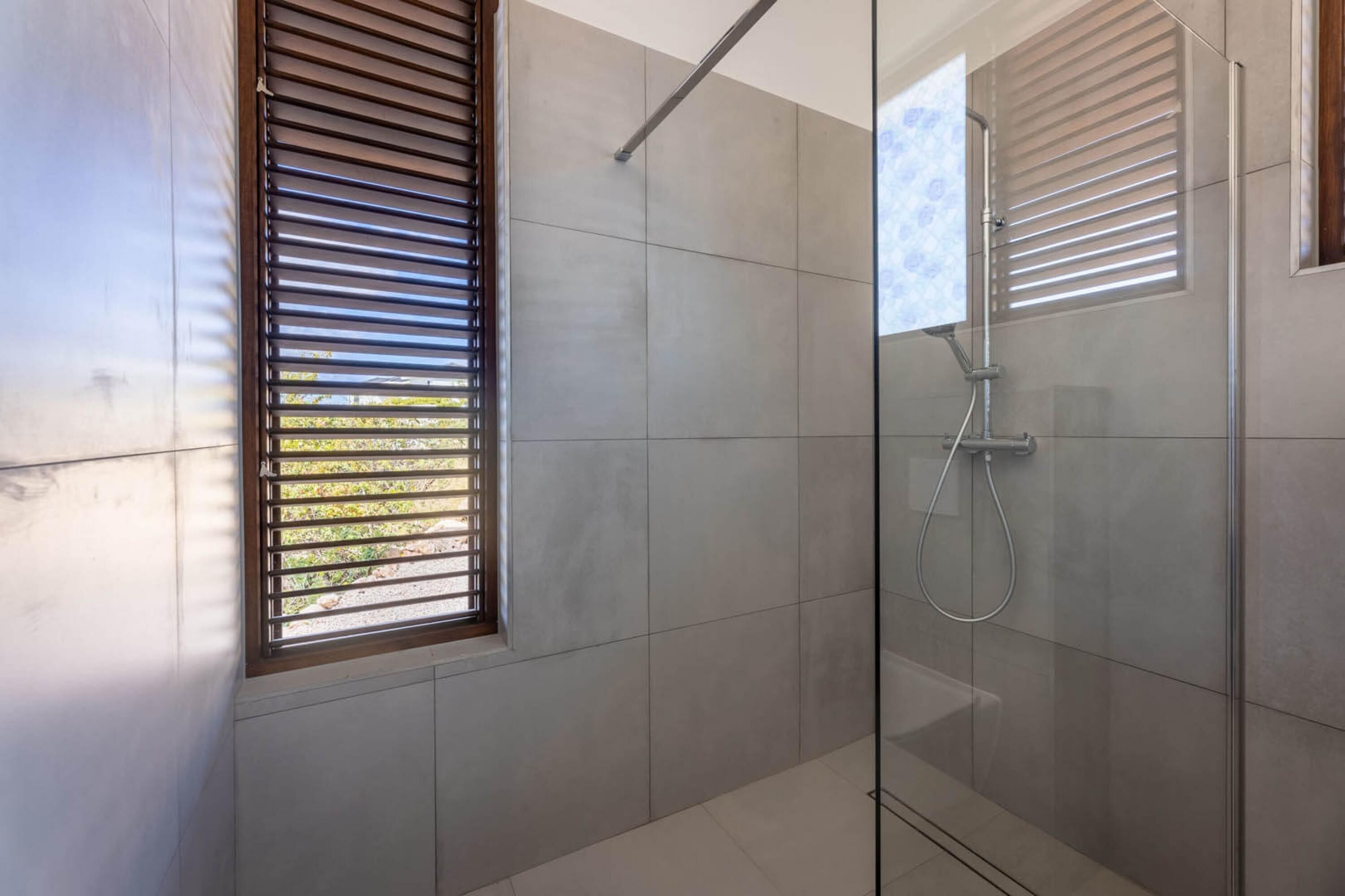 A modern bathroom with a glass-enclosed shower, tiled walls, and a window with blinds.