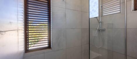 A modern bathroom with a glass-enclosed shower, tiled walls, and a window with blinds.