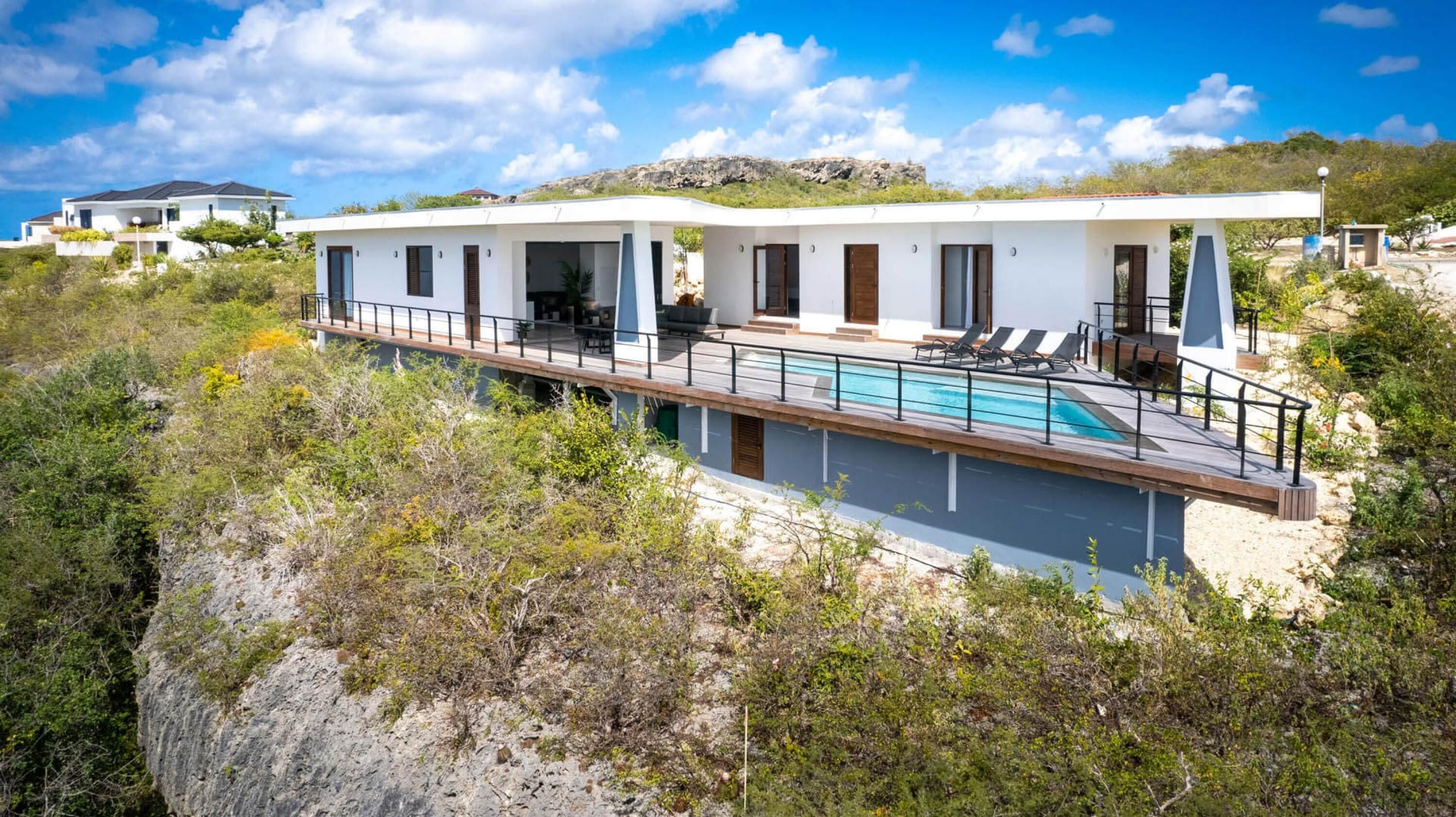 Eine moderne Villa mit Pool, mehreren Zimmern und Blick auf die umliegende Landschaft.