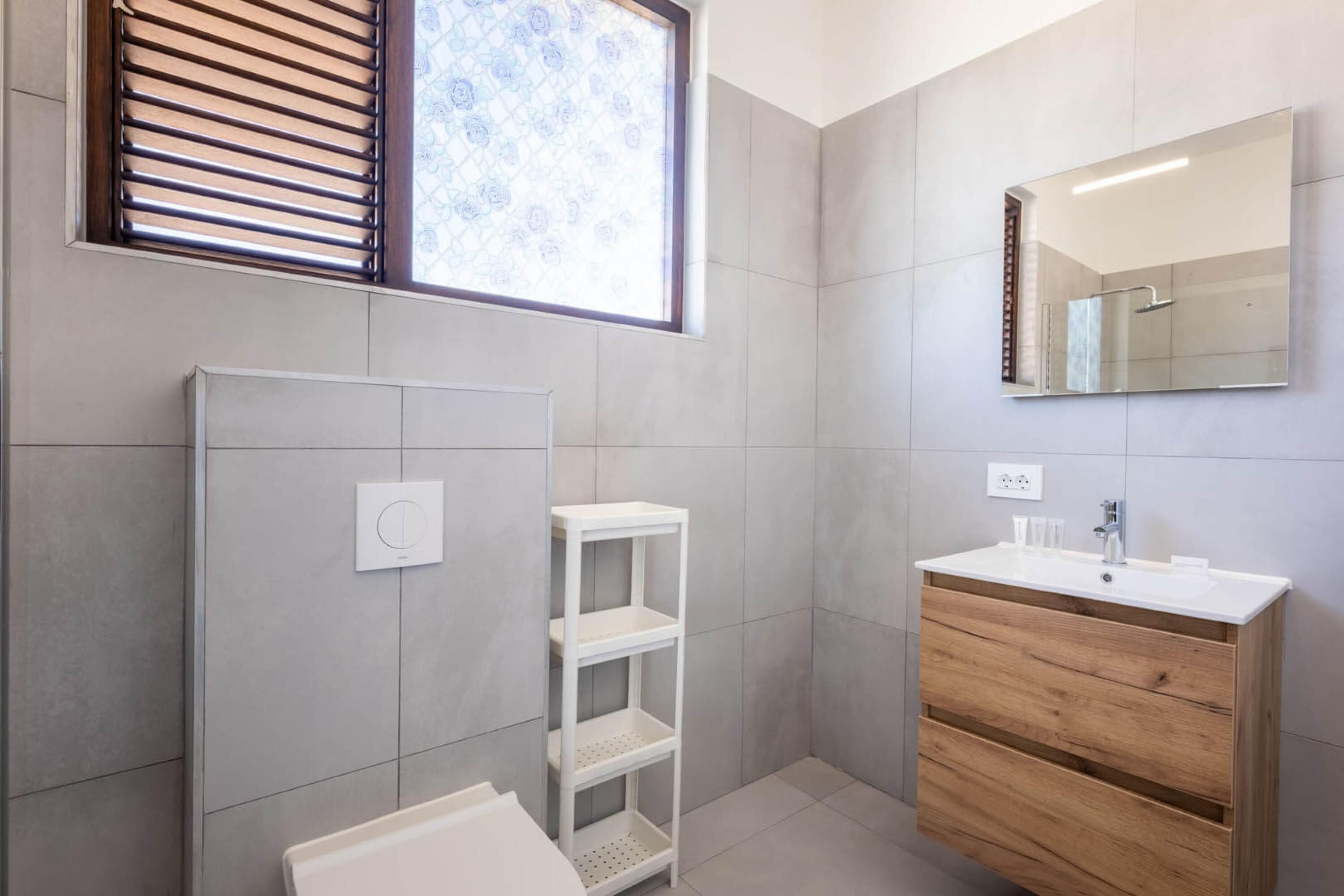 A modern bathroom with a white vanity, a mirror, and a shelf unit.