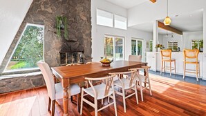 A dining area with a wooden table and chairs, a stone fireplace, and a view of a garden through a large window. - Charming Retreat near Healdsburg – 3 BD + Den, Outdoor Dining (Healdsburg)