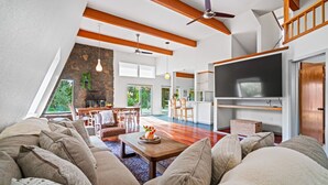 A spacious living room with a wooden ceiling, a stone accent wall, and a dining area with a large TV. - Charming Retreat near Healdsburg – 3 BD + Den, Outdoor Dining (Healdsburg)