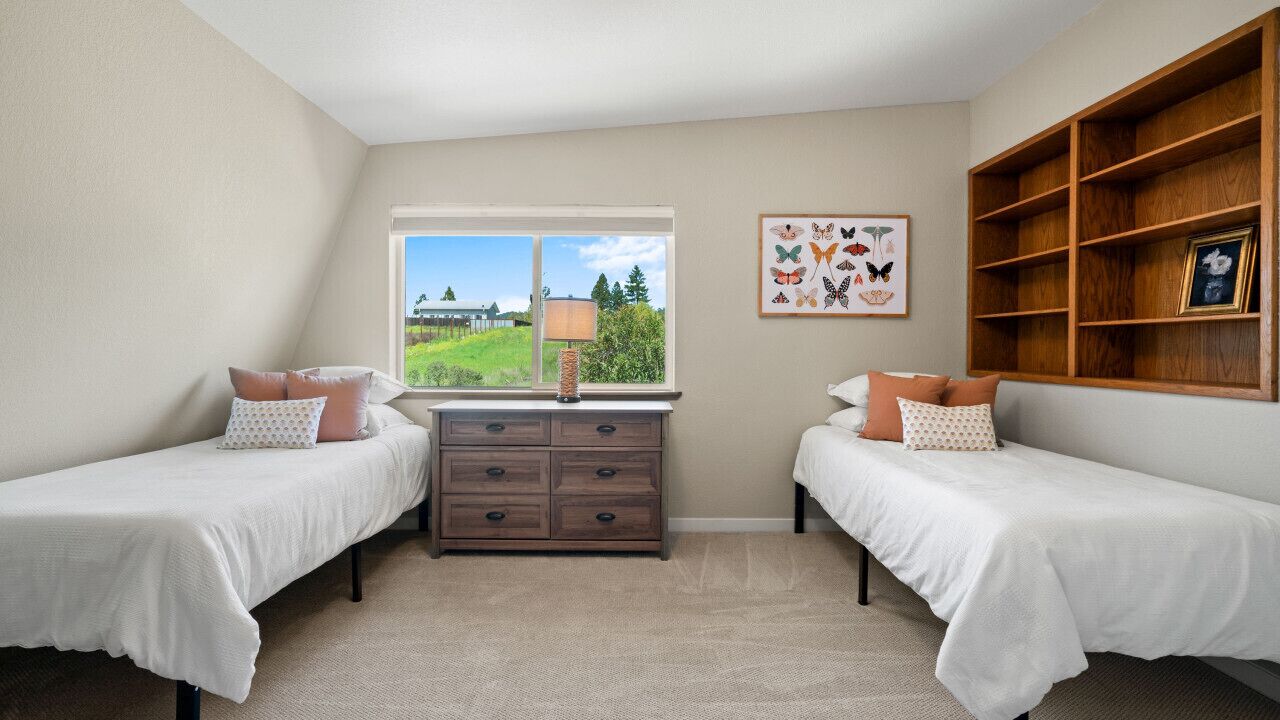 A bedroom with two beds, a dresser, a window with a view, and a wooden shelf with a picture frame.