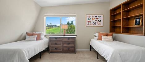 A bedroom with two beds, a dresser, a window with a view, and a wooden shelf with a picture frame.