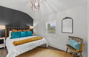 Une chambre à coucher avec un plafond incurvé, un lit avec de nombreux oreillers, un banc en bois, un miroir et une fenêtre.