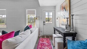 Een kamer met een witte bank, kleurrijke kussens, een rood vloerkleed, een zwarte console tafel en een schilderij aan de muur.