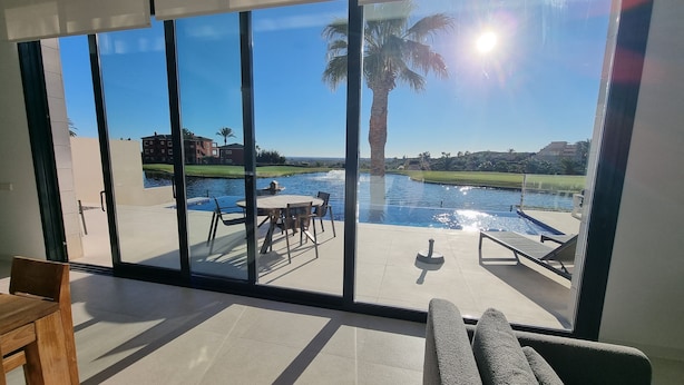 A modern room with a large sliding glass door leading to an outdoor pool area with a view of a body of water and palm trees. - Moderne villa, met artistieke inrichting. dicht bij wandelpaden, zee, golfgebied (Vera)