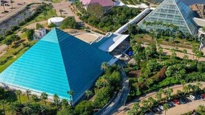 Suuri pyramidin muotoinen rakennus, jonka katto on sininen, ja jonka ympärillä on viheralueita ja parkkipaikka.