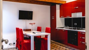 A compact kitchen with red cabinets, a white table, and red chairs.