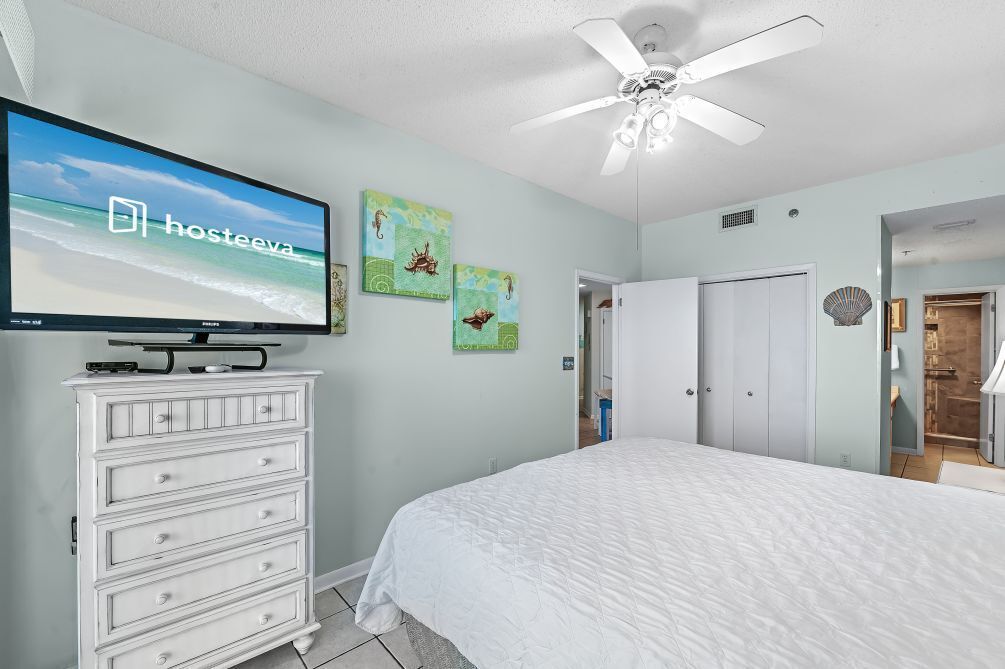 Ein Schlafzimmer mit einem Bett, einem Fernseher auf einer Kommode, einem Deckenventilator und einem Kunstwerk an der Wand.