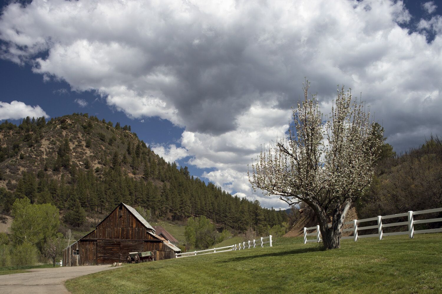 A rustic barn with a white fence in a rural setting.