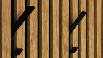 A wooden wall with vertical planks and two black metal hooks.