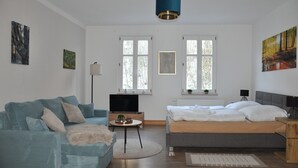 A modern, well-lit room with a sofa, a bed, a TV, and artwork on the walls. - Ferienwohnung Gerberstein (Ruhla)