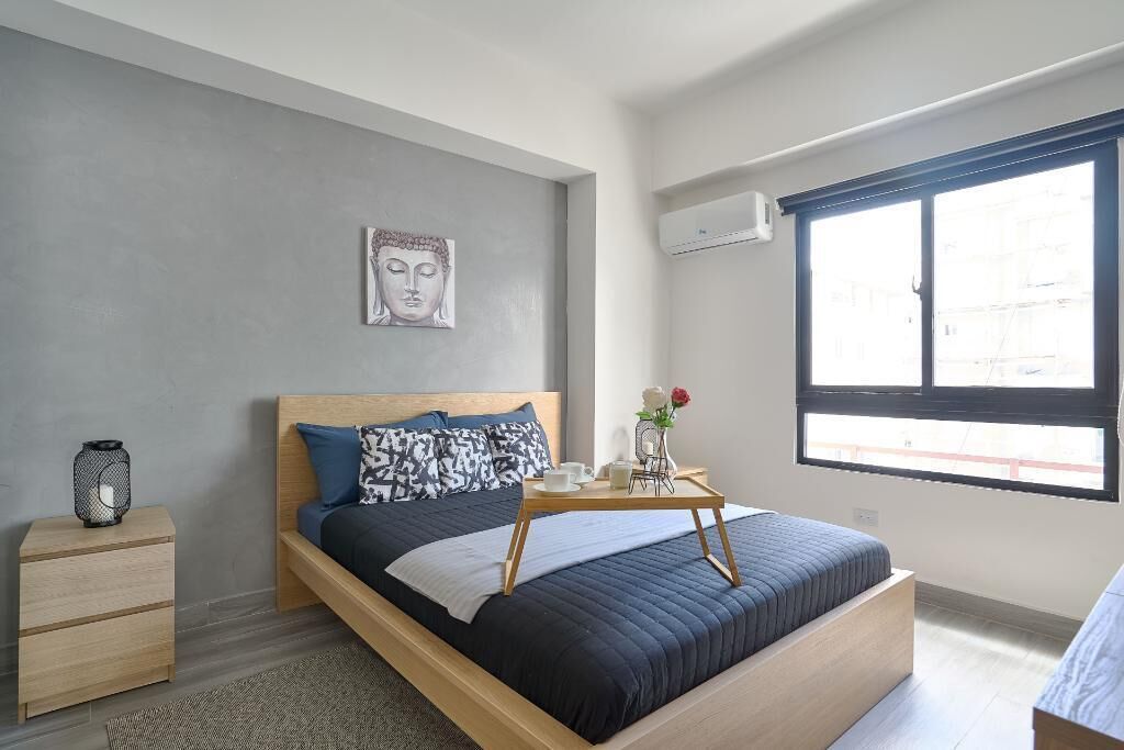 A modern bedroom with a bed, bedside table, and a window with blinds.