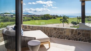 A balcony with a stone wall, a cushioned chair, and a view of a golf course and buildings in the distance. - Lux Ocean & Bay Views, Full Access, 2 Golf Carts, Plunge Pool, Cook/Cleaning (Punta de Mita)