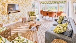 Ein Wohnzimmer mit Sofa, Sesseln, Couchtisch, Fernseher und einer Wand mit Muster.