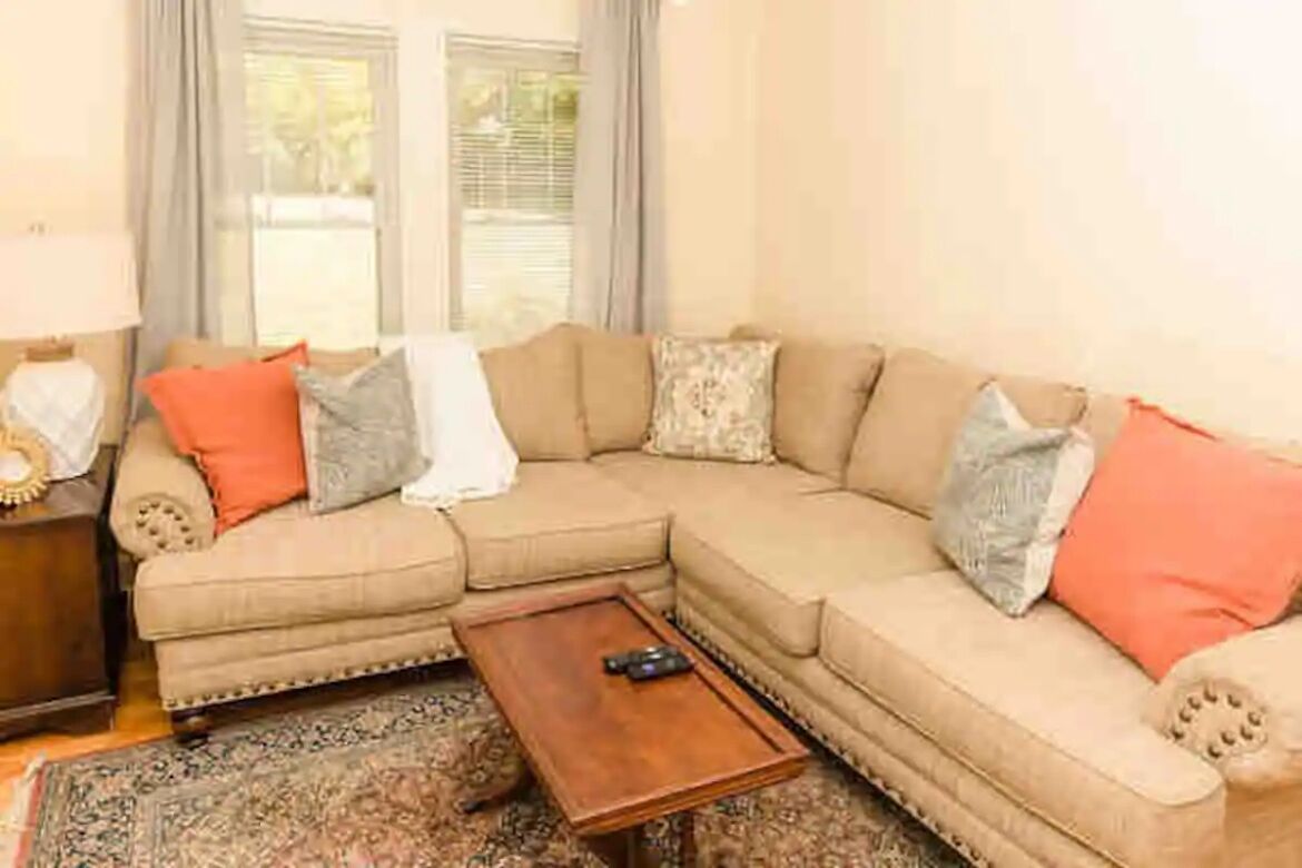 Un salon avec un canapé d’angle beige, une table basse en bois et un tapis à motifs.