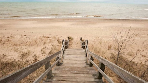 Une promenade en bois mène à une plage de sable, avec l’océan en arrière-plan.